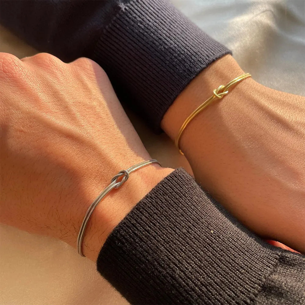 Two wrists side by side in sunlight, each wearing a knot bracelet, one gold and one steel